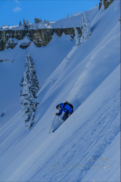A skier in blue carves effortlessly down the steep, powder-laden flank of Glory Bowl, sunlight glancing off crystalline snow under an endless western sky. In this high country—where Teton Valley spills into the shadow of the Range, and Jackson Hole lies cradled between mountain giants—the air crackles with winter’s clarity. Every turn stirs centuries-old snow ghosts clinging to whitebark pines; each breath carries a trace of cold sage from distant flats where bison roam below. The Greater Yellowstone region sprawls beyond sight, shaped by fire and ice, its vastness both wild sanctuary and skiers’ playground—where ambition rides side by side with humility before raw nature. Here in this moment—a streak of blue against alpine brilliance—the skier is part of something far older than trails or towns: a living pulse at the heart of the Tetons’ unforgettable winter canvas.